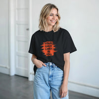 Load image into Gallery viewer, Woman wearing a black t-shirt with an orange motivational quote in a minimal indoor setting
