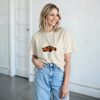 Load image into Gallery viewer, Woman wearing a beige t-shirt with a car graphic and light blue jeans indoors.
