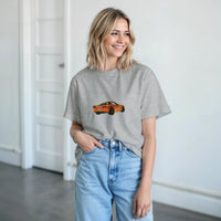 Load image into Gallery viewer, Woman wearing a gray t-shirt with a car graphic and light blue jeans indoors.
