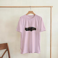 Load image into Gallery viewer, Pink t-shirt with a car graphic on a wooden hanger against a beige wall.
