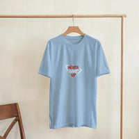 Load image into Gallery viewer, Light blue t-shirt with &#39;NEVER GIVE UP&#39; text on a wooden hanger against a beige wall.
