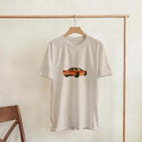 Load image into Gallery viewer, Beige t-shirt with orange car graphic on a wooden hanger against a white wall.
