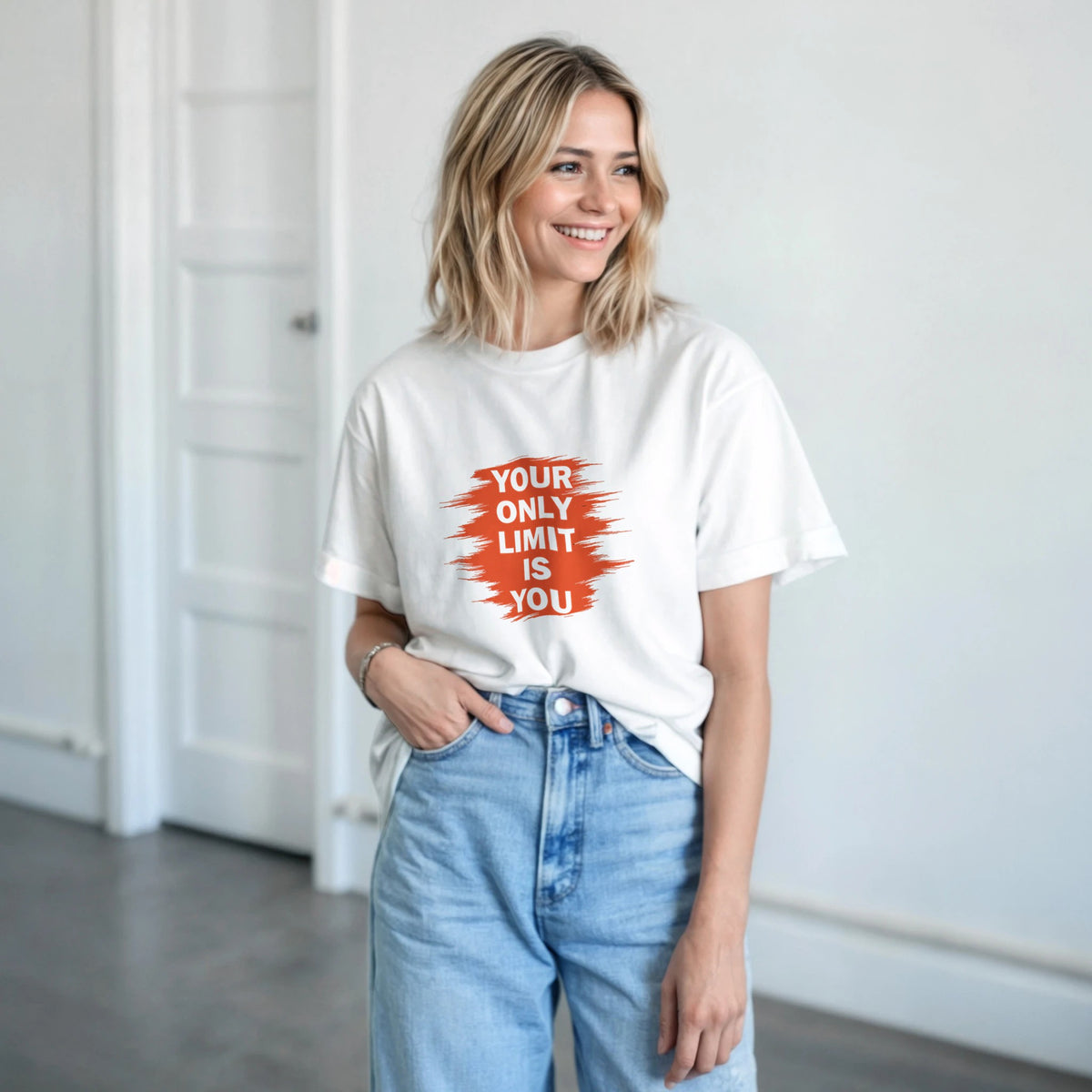 Woman wearing a white t-shirt with an motivational quote, standing in a minimalistic room.