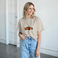 Load image into Gallery viewer, Woman wearing a beige t-shirt with a car graphic and light blue jeans indoors.
