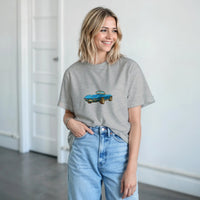 Load image into Gallery viewer, Woman wearing a gray t-shirt with a blue car graphic and light blue jeans indoors.
